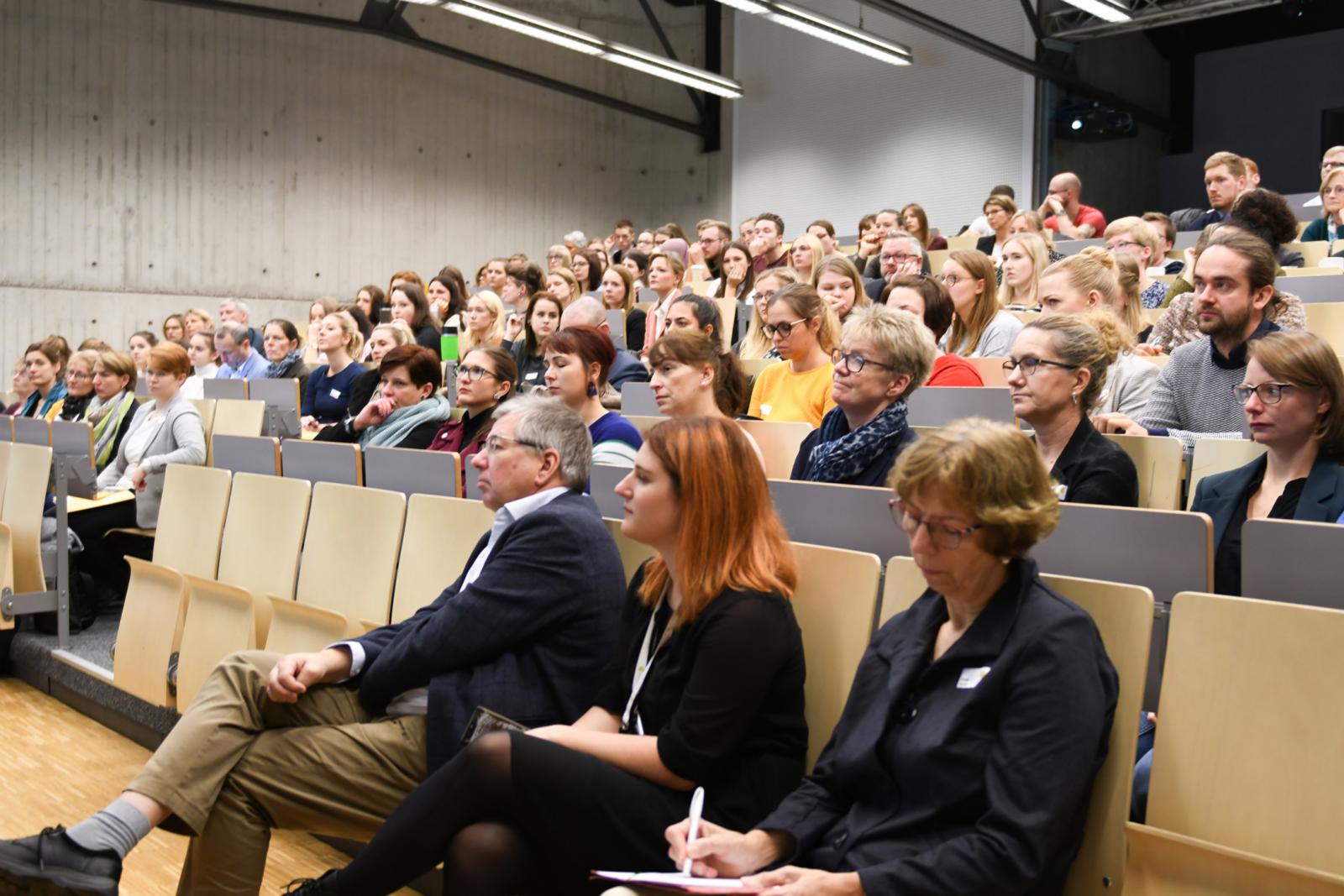 Die 320 Teilnehmerinnen und Teilnehmer verteilten sich auf mehrere Räume, die Eröffnungsvorträge wurden dorthin übertragen. Hier hören unter anderem Prof. Dr. Rüdiger Ostermann (l.) und DGP-Vorstandsvorsitzende Prof. Dr. Renate Stemmer (r.) zu. (FH Münster/Katharina Kipp)