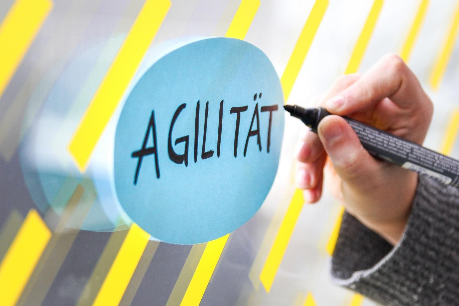 Das Wort Agilität wird auf eine Karte an einer Wand geschrieben.