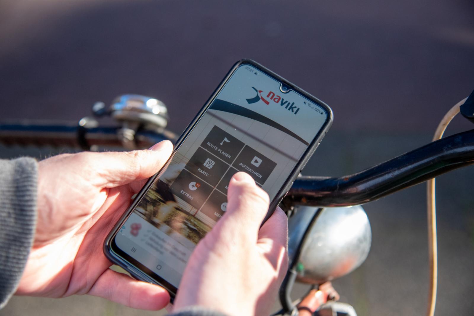 Geöffnete Naviki-App auf einem Smartphone, gehalten von einer Person auf einem Rad.