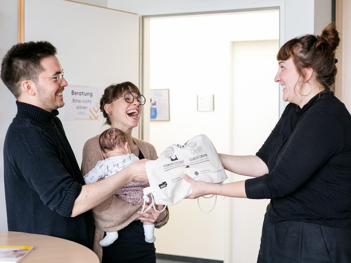 Junge Familie mit Baby bekommt Glückstasche überreicht vom Familienservice