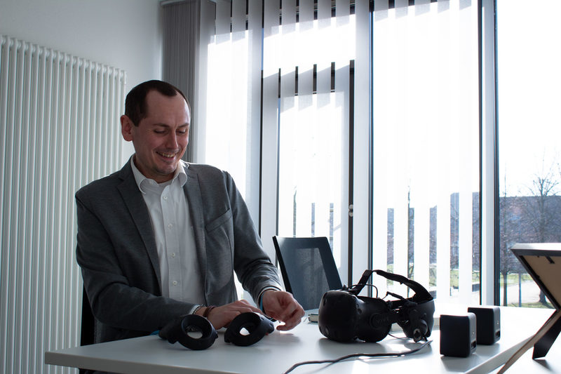 Prof. Dr. Lars Christian Grabbe am Schreibtisch mit diversen VR-Artefakten