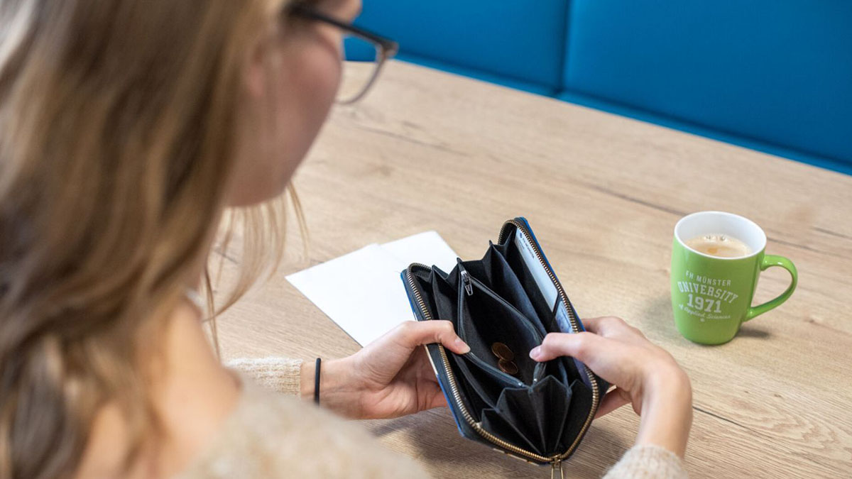 Eine Studentin blickt in ihren Geldbeutel, er ist leer. 